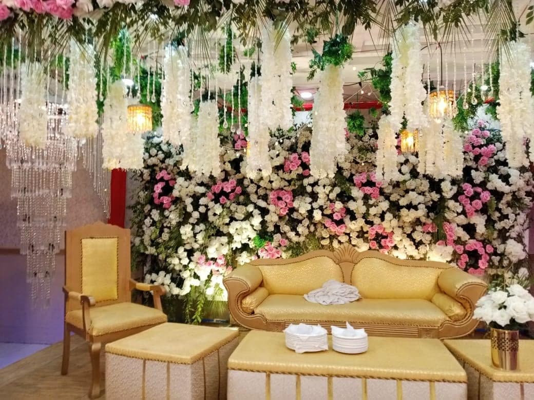 Wedding stage at Ahmed Palace with a gilded sofa beneath a wall of pink and white roses and hanging floral garlands